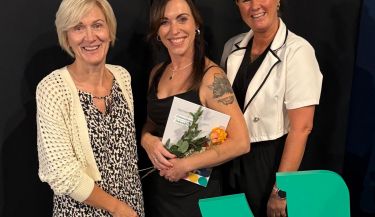 Zu sehen ist Peggy Pinkert mit ihrem Zeugnis, einer Blume und den beiden zentralen Praxisanleiterinnen.