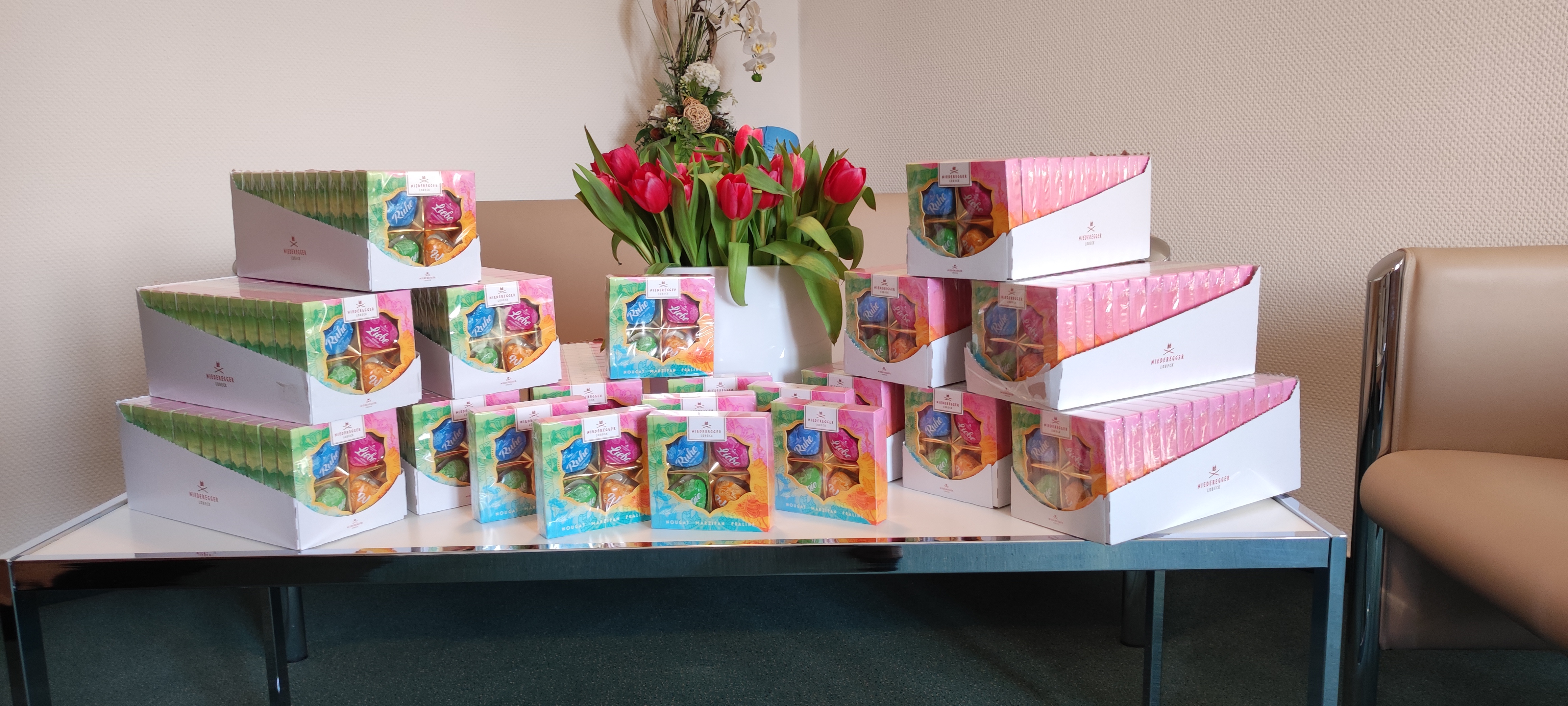 Zu sehen sind die arrangierten Pralinenpackungen mit einem Strauß Tulpen.